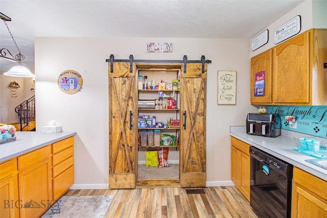 kitchen featuring decorative light fixtures, a barn door, light hardwood / wood-style floors, and black dishwasher