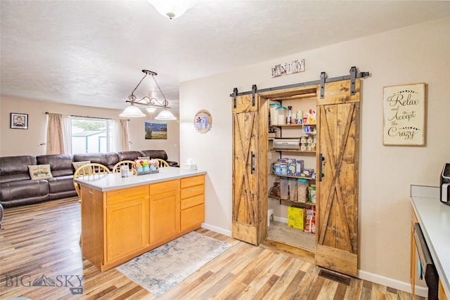 kitchen with kitchen peninsula, pendant lighting, a barn door, and light hardwood / wood-style flooring