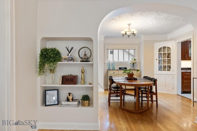 dining space with hardwood / wood-style floors, built in shelves, a textured ceiling, and a chandelier