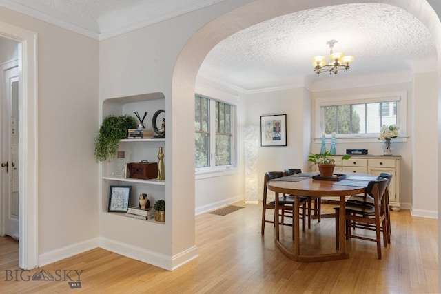 dining space featuring a textured ceiling, light hardwood / wood-style floors, crown molding, and a chandelier