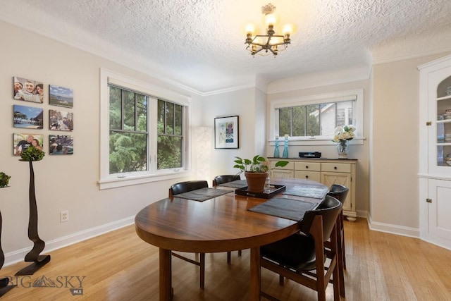 dining room with a textured ceiling, light wood-type flooring, ornamental molding, and a chandelier