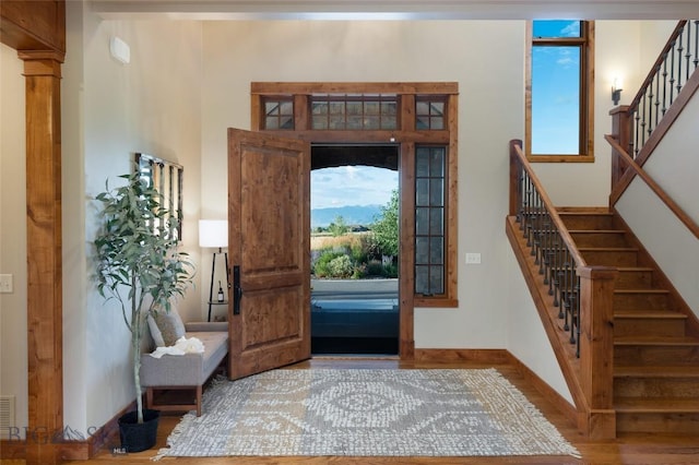 entrance foyer with decorative columns, baseboards, a towering ceiling, wood finished floors, and stairs