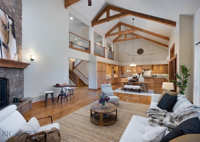 living area featuring light wood-style flooring, beamed ceiling, a stone fireplace, and stairs