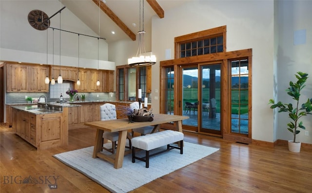 kitchen featuring a kitchen island with sink, light wood-style floors, backsplash, light stone countertops, and pendant lighting