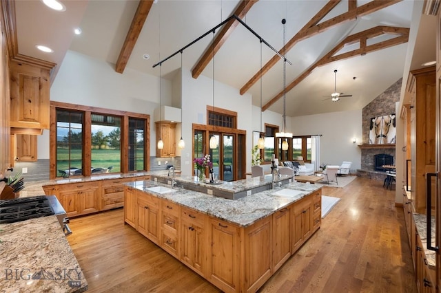 kitchen featuring a large island, open floor plan, hanging light fixtures, light stone countertops, and a sink