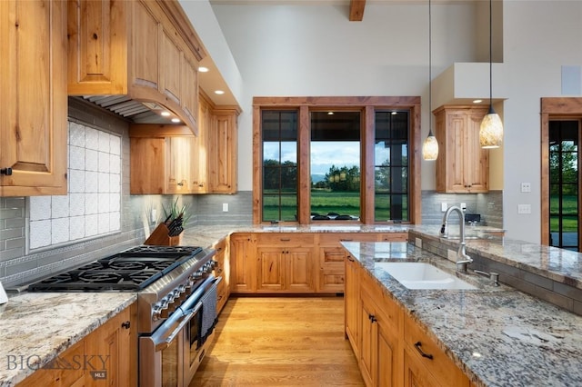 kitchen featuring high end stove, light stone countertops, a sink, and decorative light fixtures