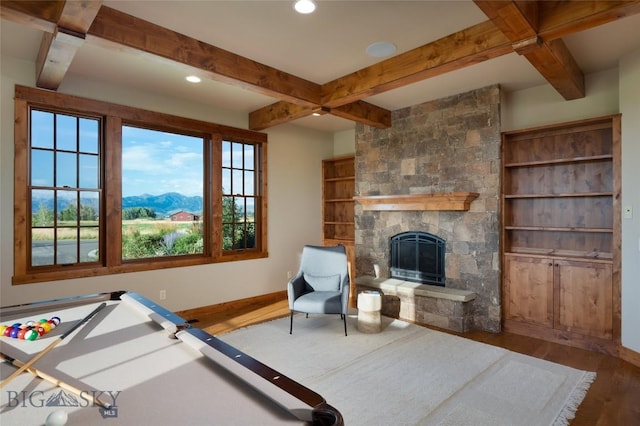 recreation room with baseboards, beamed ceiling, wood finished floors, a stone fireplace, and a mountain view