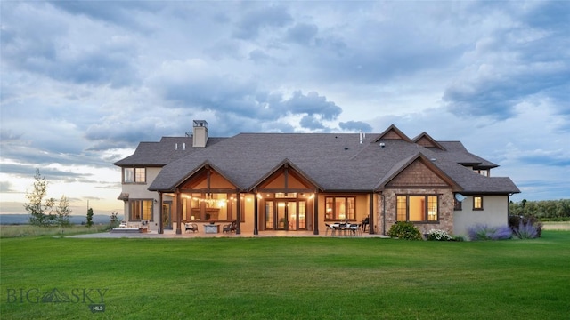 back of house with a yard, a patio, a chimney, and a shingled roof