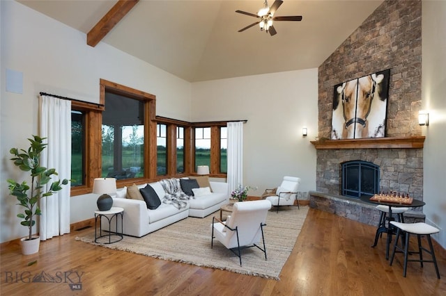 living area with beam ceiling, ceiling fan, a stone fireplace, wood finished floors, and high vaulted ceiling