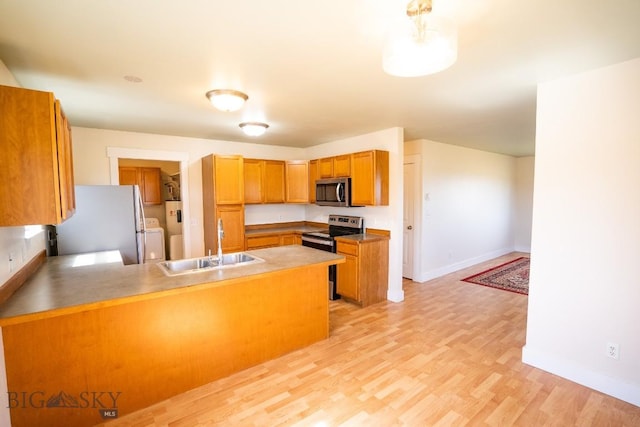 kitchen featuring brown cabinets, a peninsula, stainless steel appliances, light wood-type flooring, and a sink