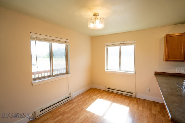 unfurnished dining area featuring a baseboard heating unit, baseboards, and light wood-style floors