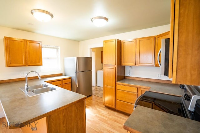 kitchen featuring a peninsula, appliances with stainless steel finishes, brown cabinetry, and a sink