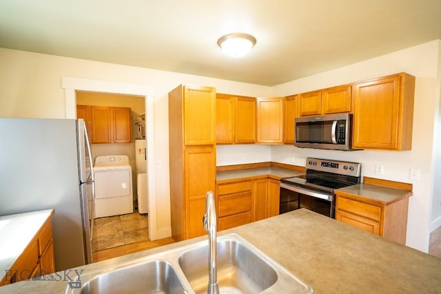 kitchen with brown cabinetry, appliances with stainless steel finishes, washer / clothes dryer, and a sink