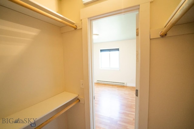 spacious closet featuring a baseboard heating unit and wood finished floors