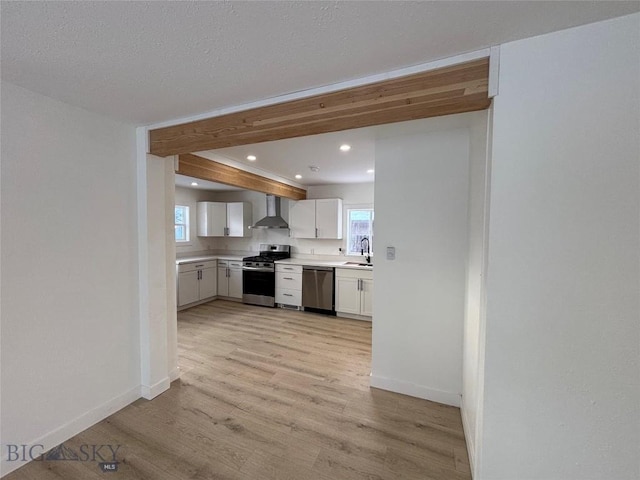 kitchen featuring a wealth of natural light, white cabinetry, wall chimney range hood, and appliances with stainless steel finishes