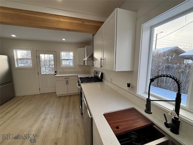 kitchen with sink, light wood-type flooring, range hood, appliances with stainless steel finishes, and white cabinetry