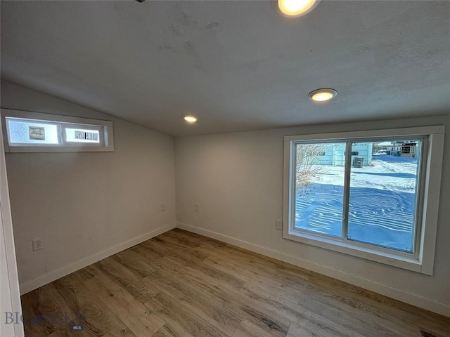 spare room featuring a healthy amount of sunlight, vaulted ceiling, and hardwood / wood-style flooring