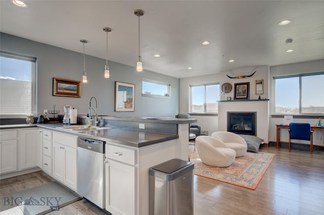 kitchen with light wood-type flooring, stainless steel dishwasher, sink, white cabinetry, and hanging light fixtures