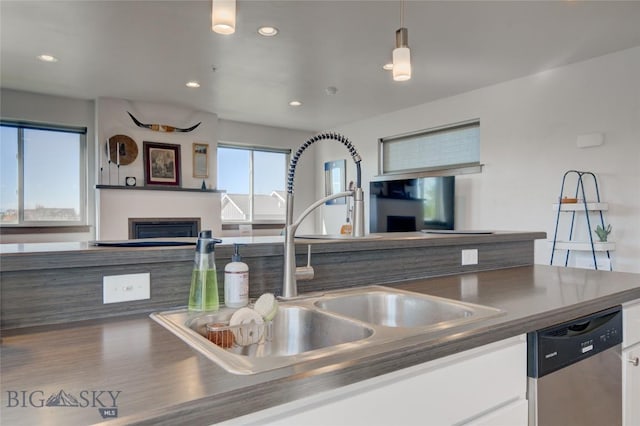 kitchen featuring stainless steel dishwasher, white cabinetry, sink, and hanging light fixtures