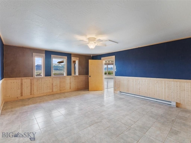 empty room featuring wooden walls, ceiling fan, and a baseboard heating unit