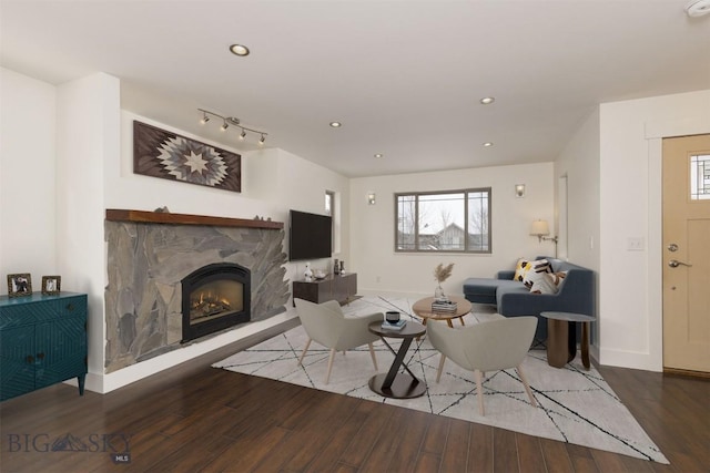 living room with hardwood / wood-style floors, a stone fireplace, and track lighting