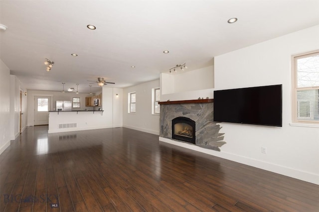 unfurnished living room featuring ceiling fan, a fireplace, dark wood-type flooring, and plenty of natural light