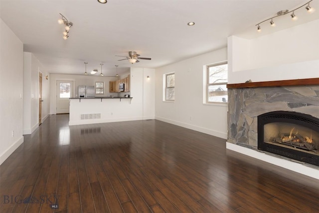 unfurnished living room featuring ceiling fan, dark hardwood / wood-style flooring, and a stone fireplace