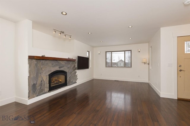 unfurnished living room with a stone fireplace, dark wood-type flooring, and track lighting