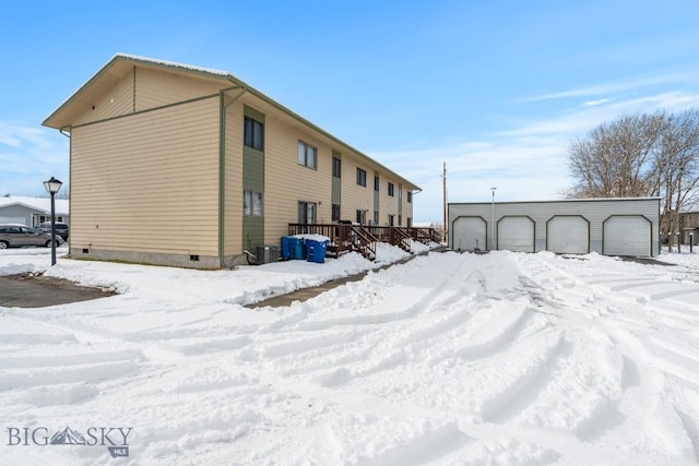 view of snowy exterior with central AC unit, a garage, and an outbuilding