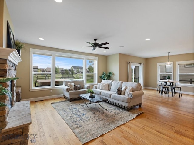 living room featuring ceiling fan, light hardwood / wood-style floors, and a stone fireplace