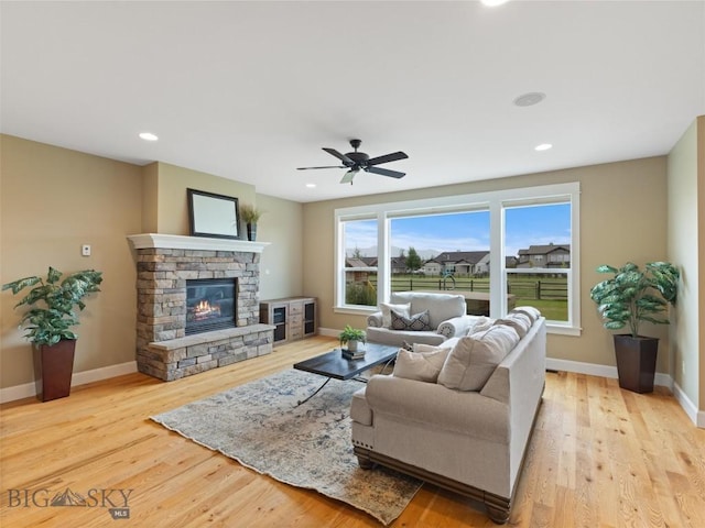 living room with ceiling fan, light wood-type flooring, and a stone fireplace