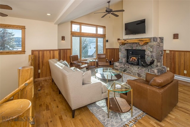 living room with vaulted ceiling, ceiling fan, a wood stove, and light wood-type flooring