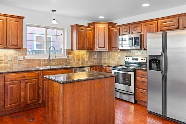 kitchen featuring sink, appliances with stainless steel finishes, dark stone countertops, hanging light fixtures, and a kitchen island