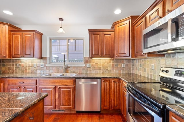 kitchen with sink, hanging light fixtures, stainless steel appliances, dark hardwood / wood-style floors, and dark stone counters