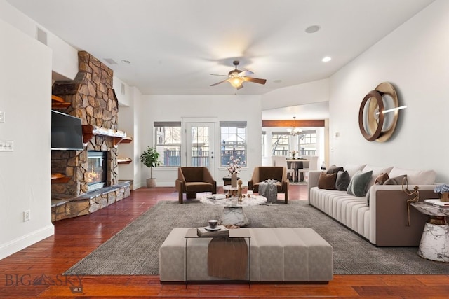 living room with dark hardwood / wood-style floors, a stone fireplace, and ceiling fan with notable chandelier