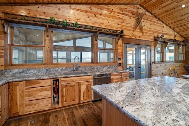 kitchen featuring light stone countertops, stainless steel dishwasher, dark wood-type flooring, wood walls, and sink