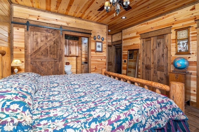 bedroom with ensuite bath, a barn door, wood ceiling, and wooden walls