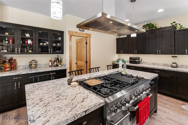 kitchen featuring light stone counters, double oven range, pendant lighting, island range hood, and light wood-type flooring