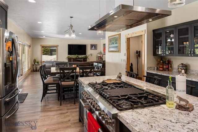 kitchen with appliances with stainless steel finishes, light hardwood / wood-style floors, ventilation hood, pendant lighting, and light stone counters