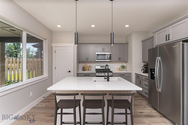 kitchen featuring a kitchen island with sink, gray cabinetry, stainless steel appliances, hanging light fixtures, and tasteful backsplash