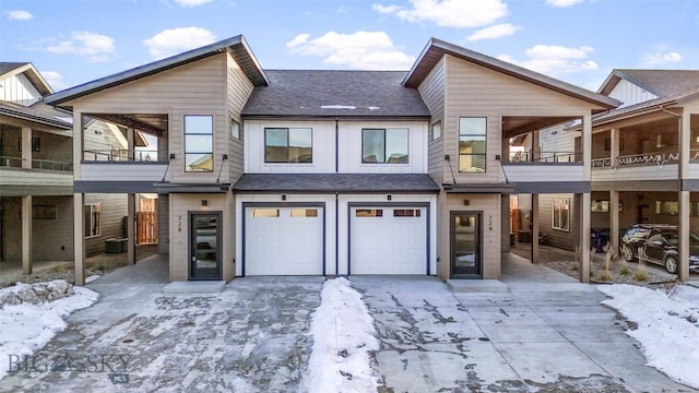 snow covered rear of property featuring a balcony, central air condition unit, and a garage