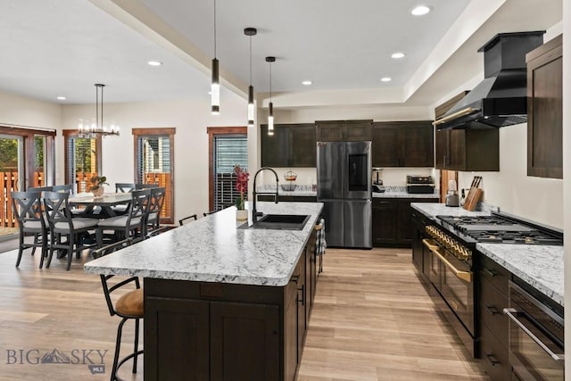 kitchen featuring double oven range, decorative light fixtures, stainless steel fridge, a kitchen island with sink, and sink