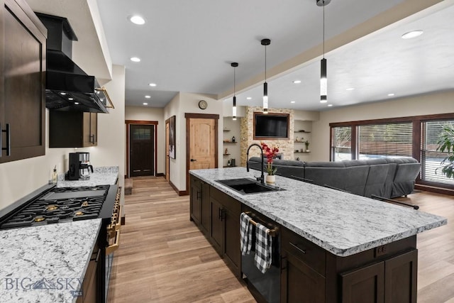 kitchen featuring decorative light fixtures, a center island with sink, high end stainless steel range, ventilation hood, and sink