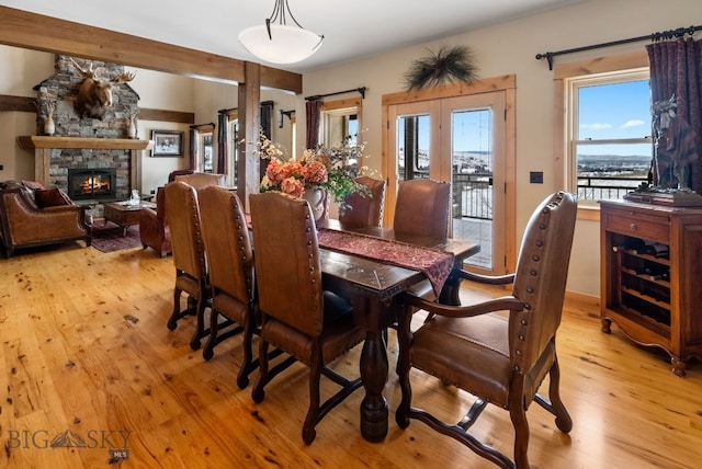 dining area with light wood-type flooring, a healthy amount of sunlight, a fireplace, and french doors