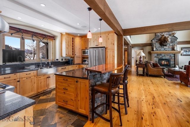 kitchen featuring beamed ceiling, a breakfast bar, a sink, open floor plan, and stainless steel appliances