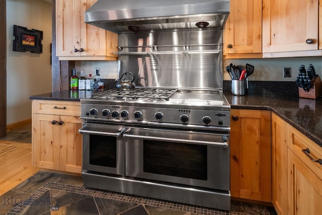 kitchen featuring dark stone countertops, range hood, and range with two ovens