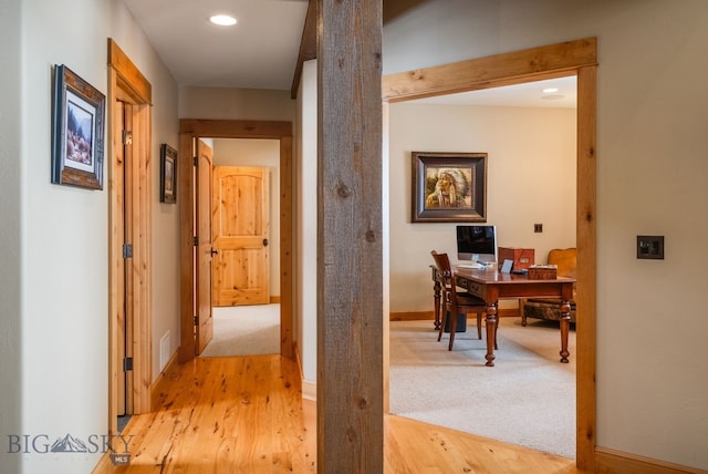 hallway featuring baseboards, light carpet, and light wood-style flooring