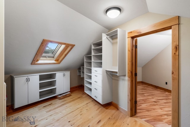 spacious closet featuring light wood-type flooring, lofted ceiling with skylight, and visible vents