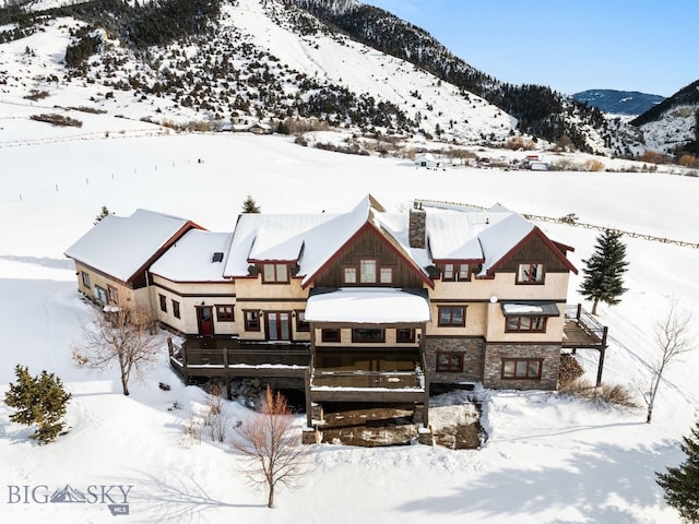 snow covered property featuring stone siding, a mountain view, and a chimney