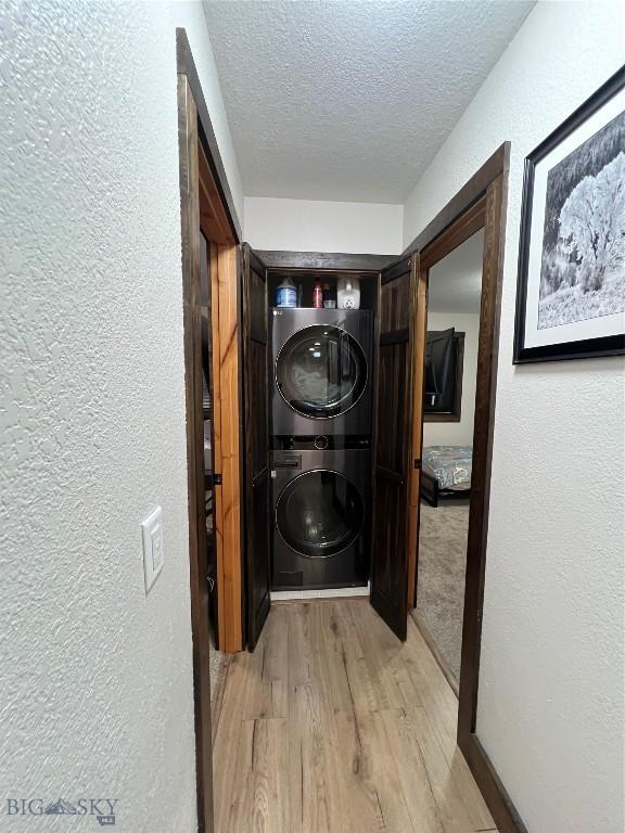 laundry area featuring stacked washing maching and dryer, a textured ceiling, and light hardwood / wood-style flooring